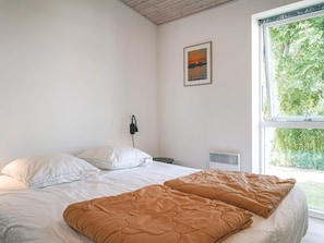 A bedroom with a bed, a window, a wall-mounted heater, and a painting. - 4 Star Holiday Home in Nexo (Nexø)