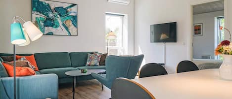 Un salon moderne avec un canapé vert, une table à manger ronde et un grand tableau abstrait accroché au mur.