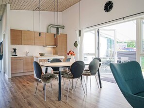 Une cuisine moderne avec des meubles en bois, une table à manger avec des chaises et une vue sur l’extérieur.