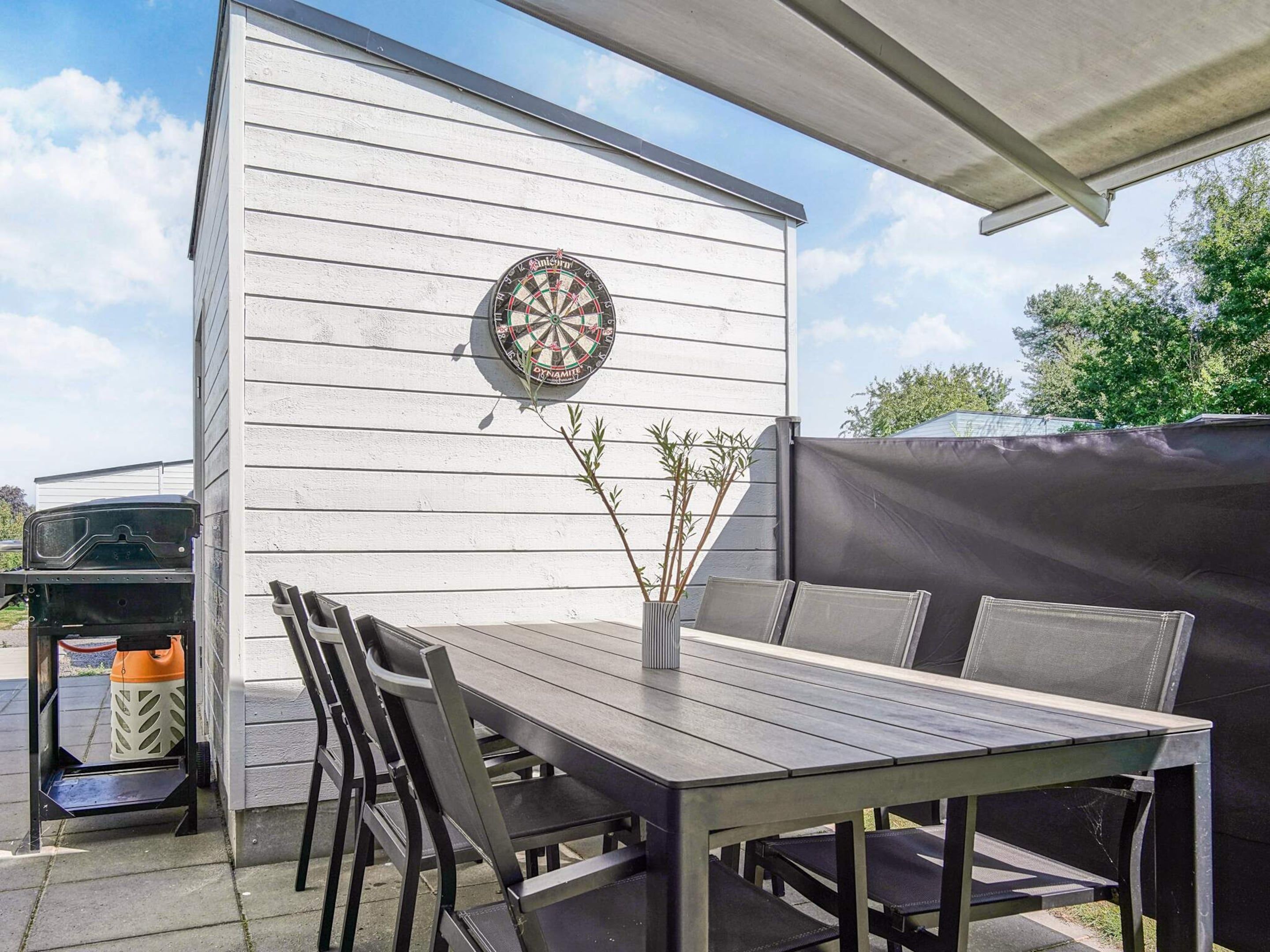 An outdoor patio with a table and chairs, a dartboard, and a covered area.