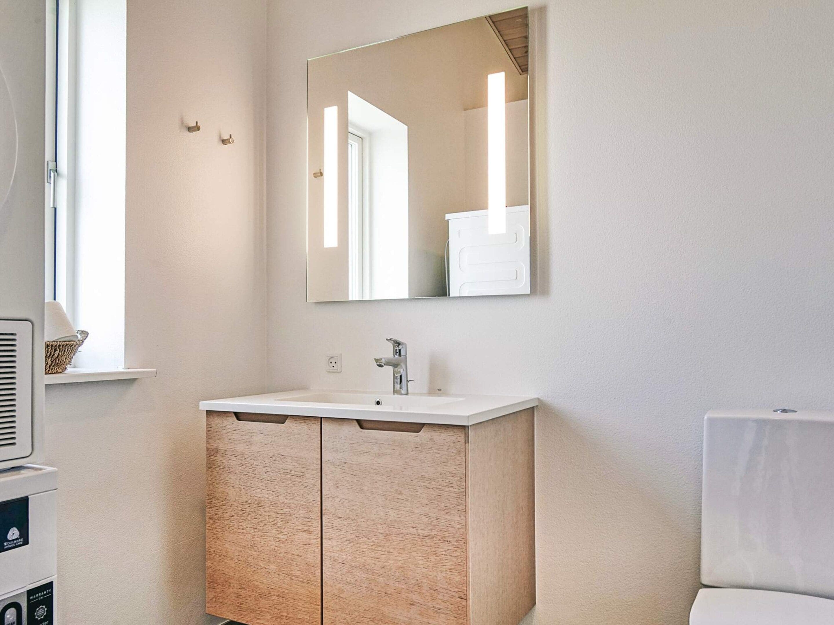 A bathroom with a white sink, a mirror, and a window.