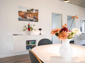 A modern room with a round table, a white cabinet with books, a painting, and a vase with flowers.