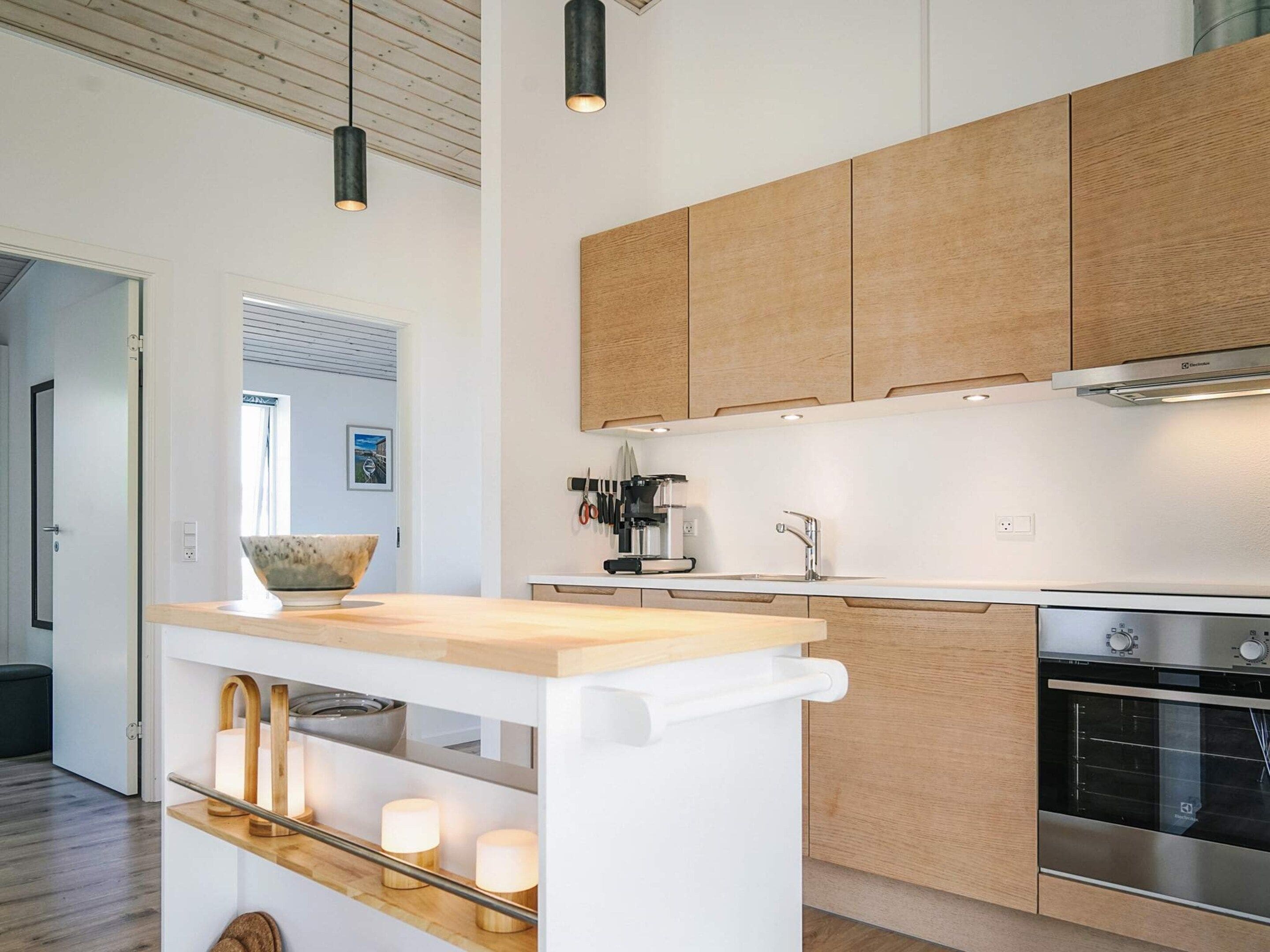 Une cuisine moderne avec des meubles en bois, un four encastré et un îlot central agrémenté d’un récipient et de bougies.