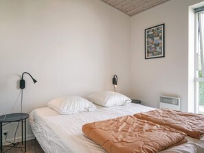 A bedroom with a bed, bedside tables, a wall-mounted lamp, a radiator, and a window. - 4 Star Holiday Home in Nexo (Nexø)