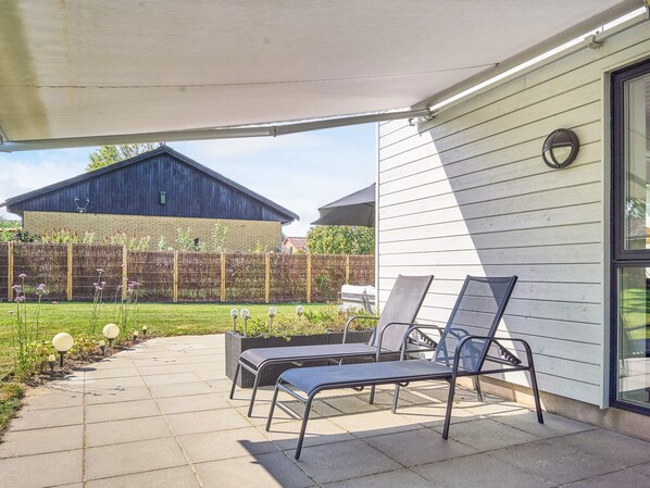 An outdoor patio area with two lounge chairs, a covered seating area, and a view of a barn and garden. - 4 Star Holiday Home in Nexo (Nexø)