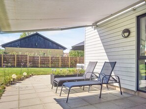A covered patio with two lounge chairs, a concrete pathway, and a wooden fence. - 4 Star Holiday Home in Nexo (Nexø)