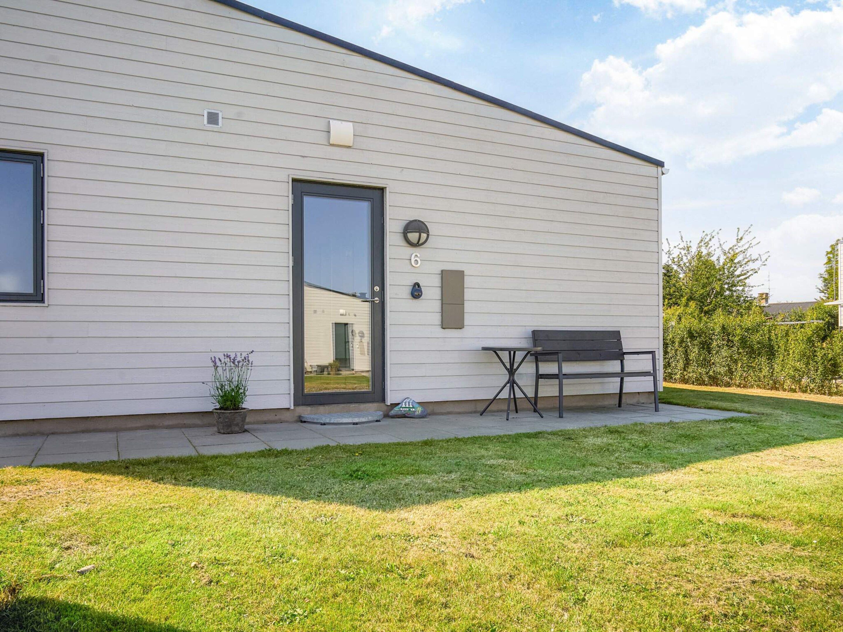 Een modern gebouw met een witte gevel, een deur, een tafeltje en een bankje.