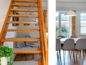 Un escalier en bois avec un arbre à chat, un coin repas avec des chaises grises et une table, et une suspension lumineuse.