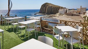 A terrace with white tables and chairs overlooking a coastal area with a rocky cliff and the sea. - Beachfront Home in La Isleta (La Isleta)