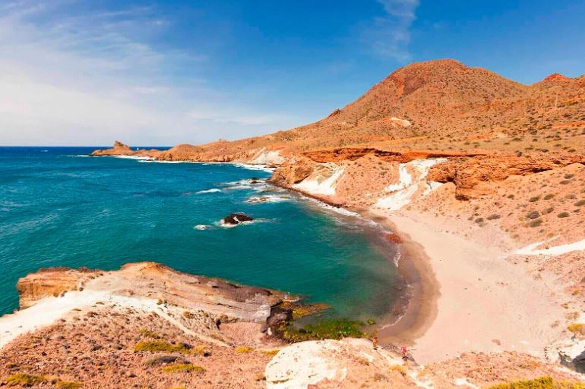 A coastal landscape with a clear sky, rocky terrain, and a beach.