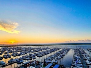 Un puerto deportivo con numerosos barcos amarrados en filas, un muelle que se adentra en el agua y un atardecer al fondo.