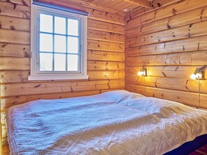 Quarto de cabana de madeira com cama, janela e duas luzes fixadas na parede.