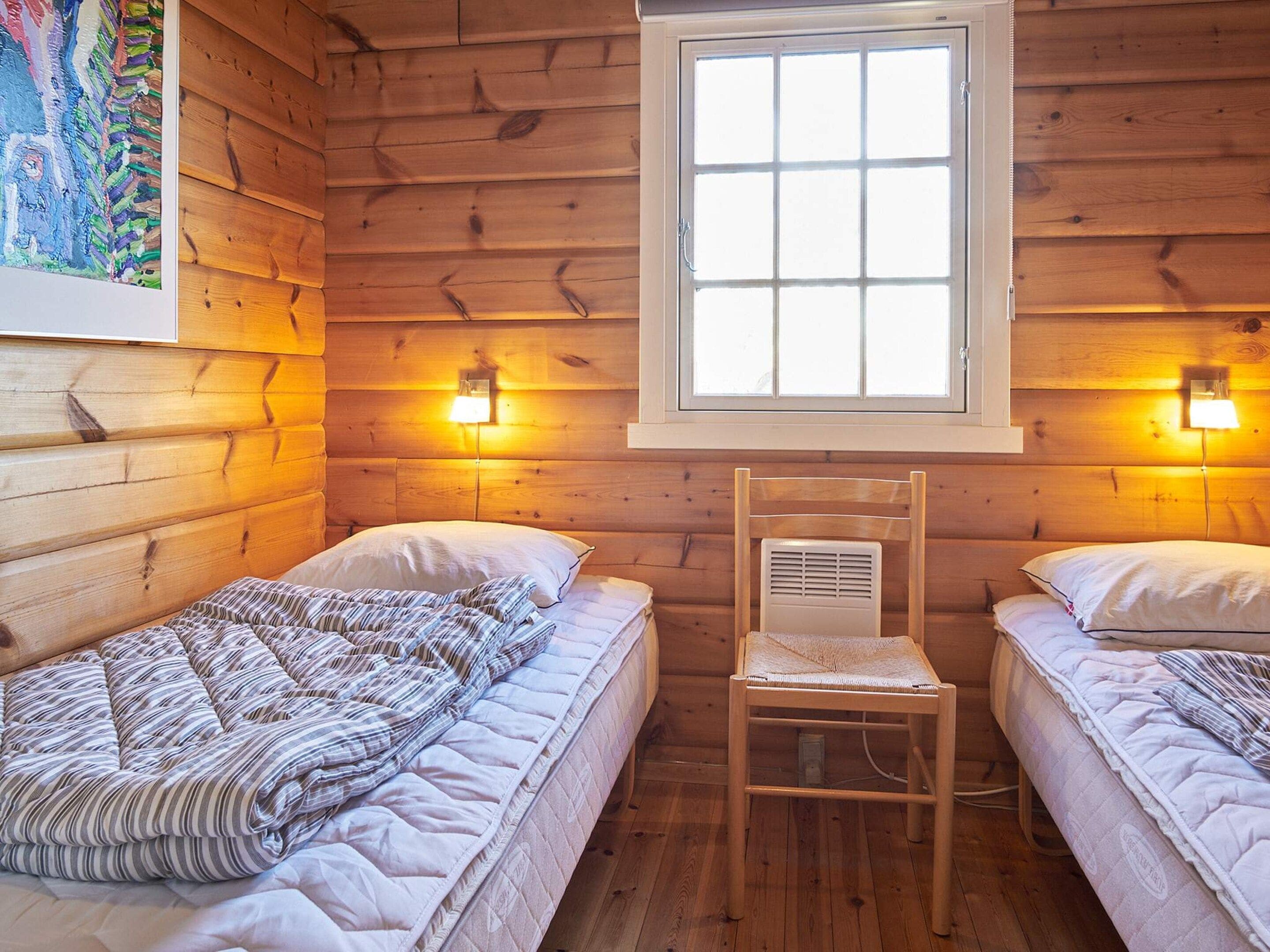 Een kamer in chaletstijl met twee eenpersoonsbedden, een houten stoel en een raam met uitzicht.
