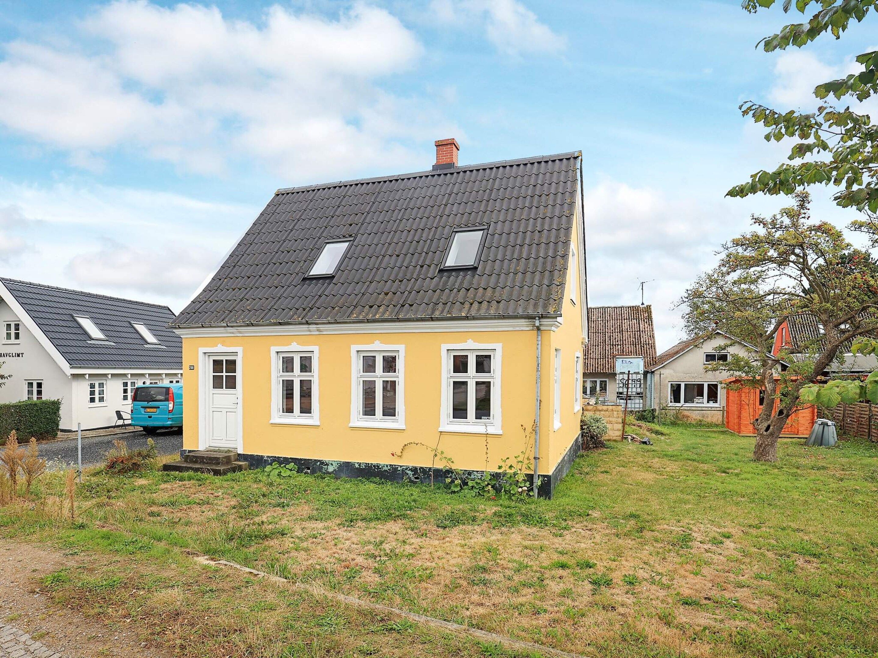 A yellow house with a grey roof, white windows, and a small porch.