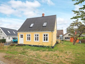 A yellow house with a grey roof, white windows, and a small porch.