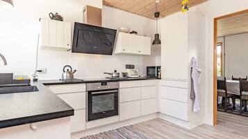 A modern kitchen with white cabinets, a built-in oven, a microwave, and a kettle.
