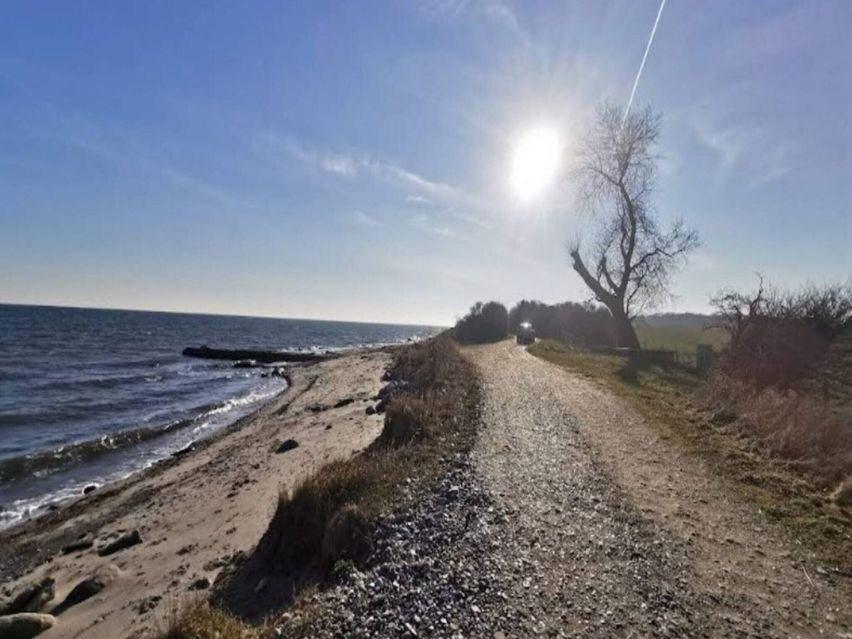 A gravel path beside a beach with the ocean and a clear sky.