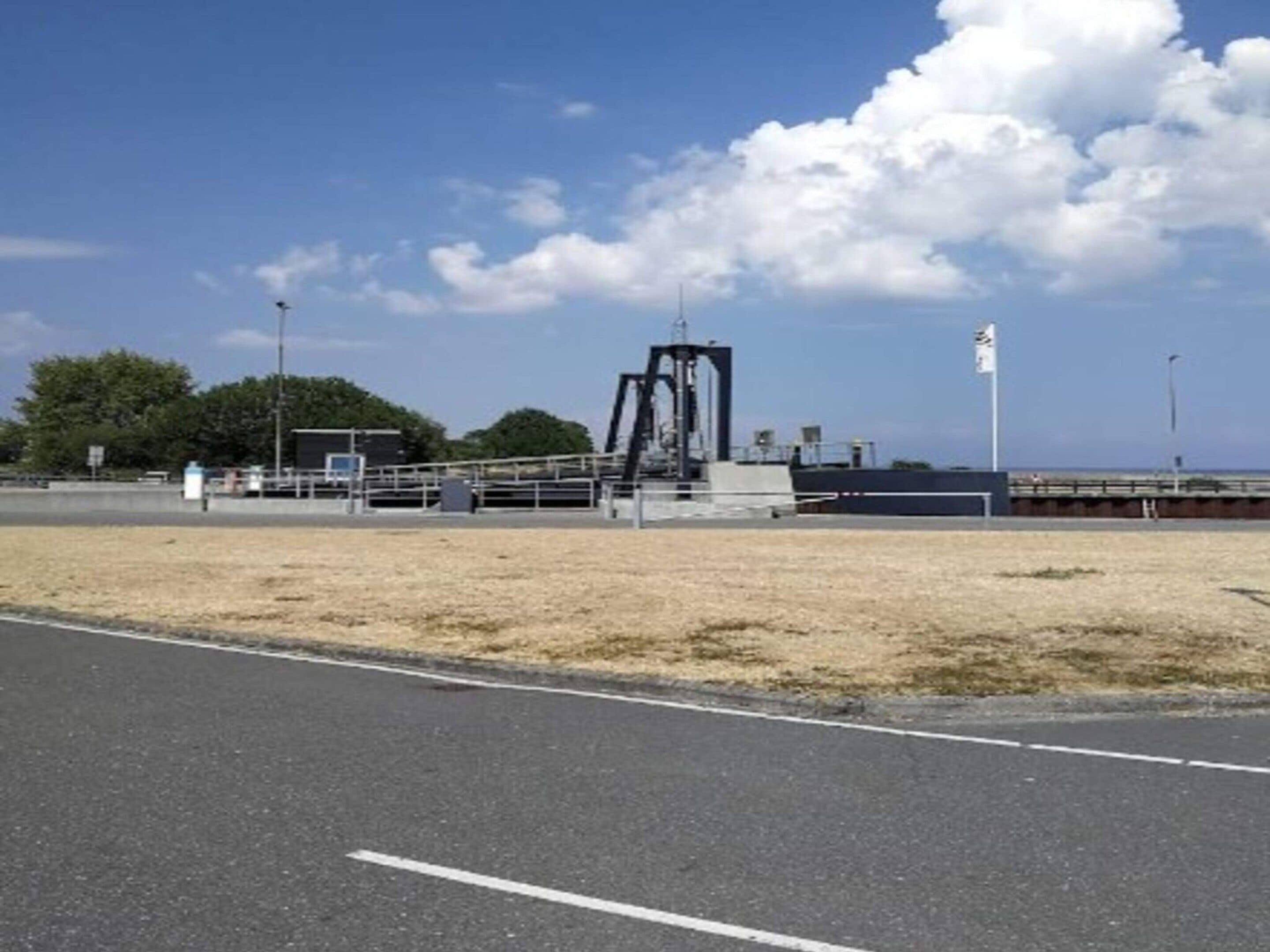 A coastal road with a metal structure, a fenced area, and a clear sky.