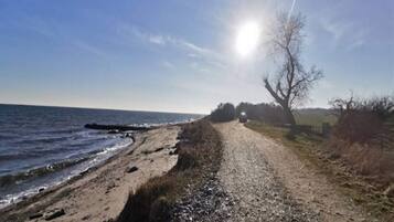 A gravel path leading to a beach with a clear sky and a sun shining.