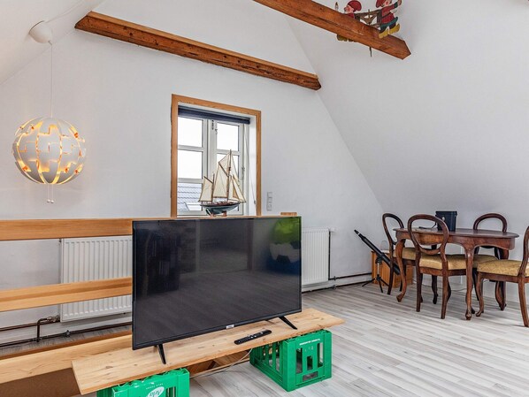 A room with a television on a wooden stand, a dining table with chairs, a window with a sailboat model, and a globe light fixture.