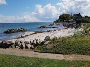 A beach with a rocky shoreline, a clear sky, and a few buildings in the background.