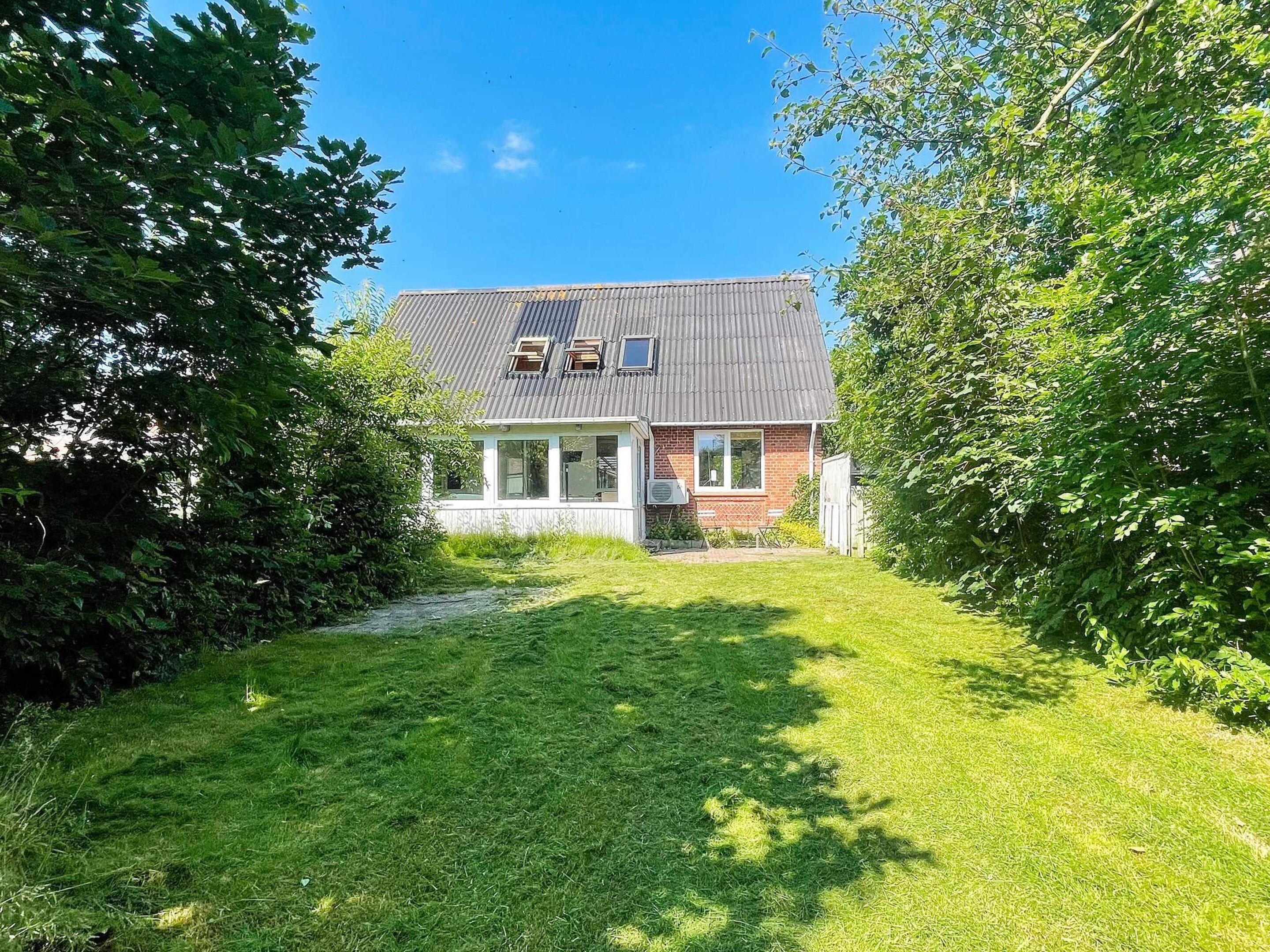 Une maison à deux étages avec un toit en pente, un porche à l’avant et un petit jardin devant la maison.
