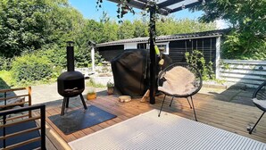 En udendørs terrasse med grill, overdækket siddeområde og en pergola med hængende lys.