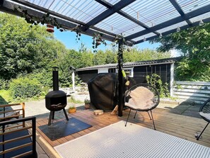 An outdoor patio with a barbecue grill, a covered seating area, and a pergola with hanging lights.