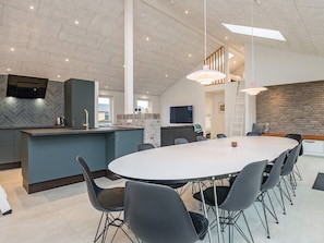A modern kitchen with a herringbone tile backsplash, a central island, and a dining area with a round table and chairs. - 12 Person Holiday Home in Lokken (Lokken)
