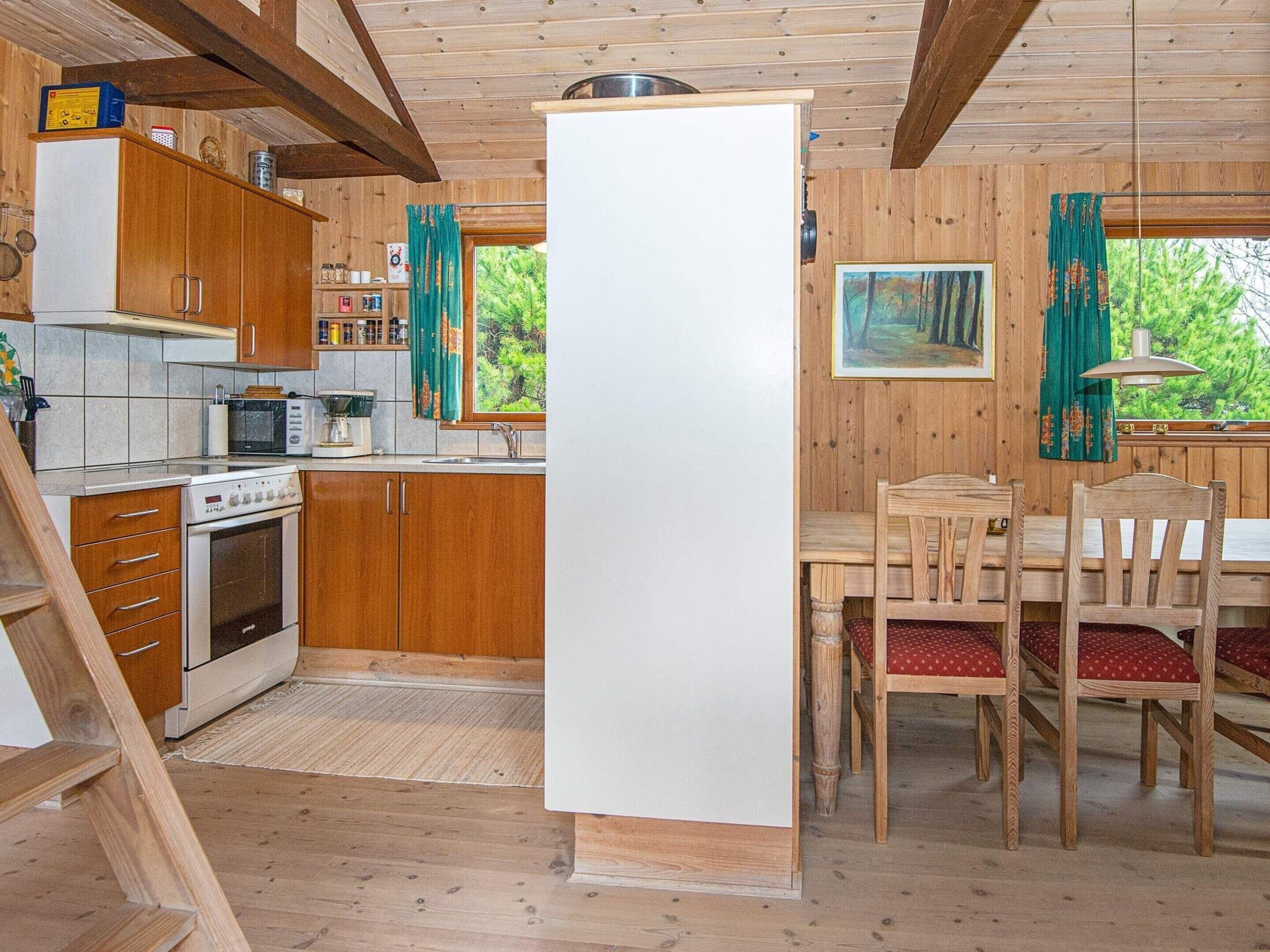 A wooden cabin with a kitchen featuring a stove, microwave, and cabinets. There is a dining table with chairs and a painting on the wall.