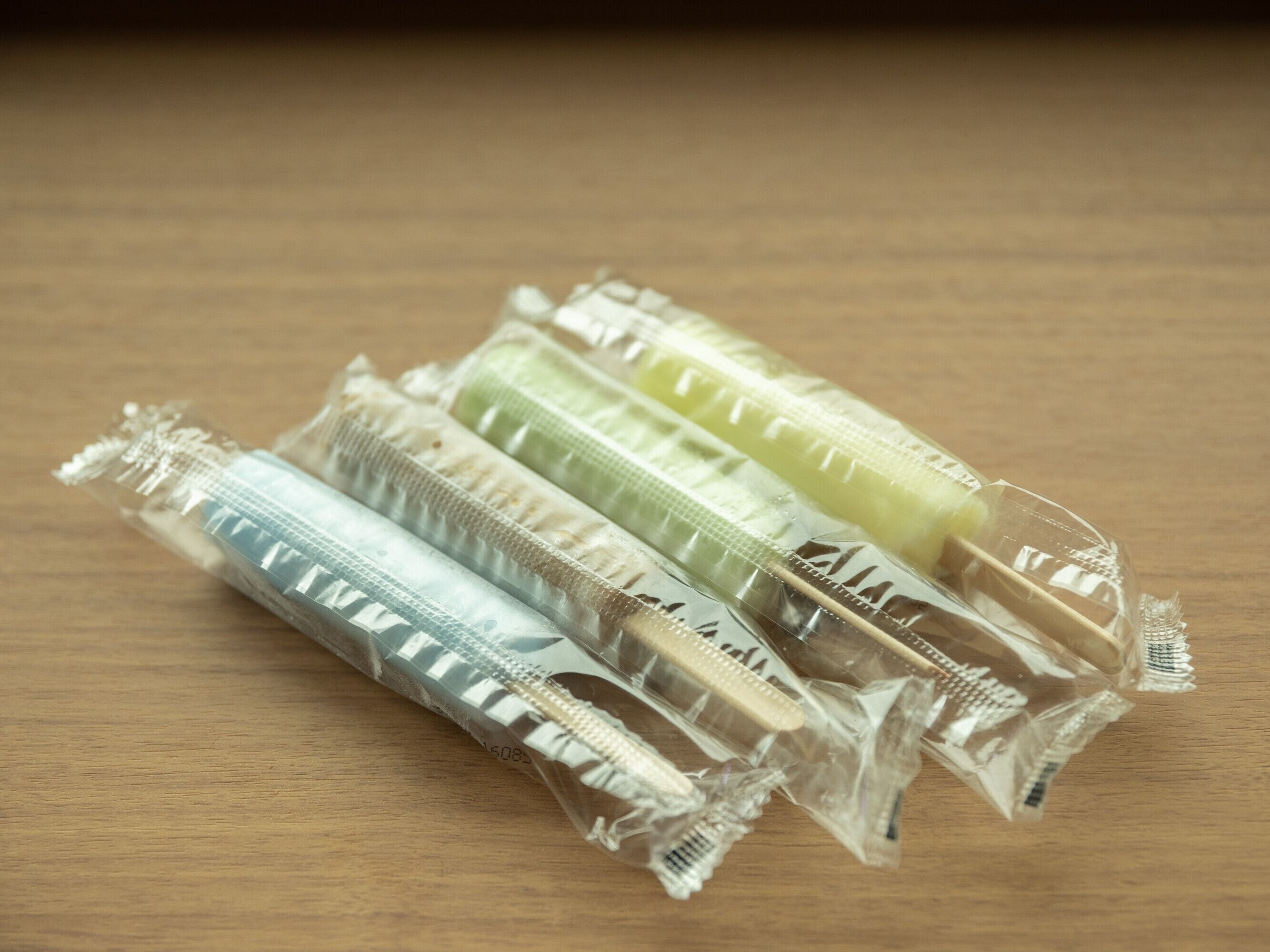 Vier Zahnbürsten in transparenter Verpackung auf einer Holztischfläche.
