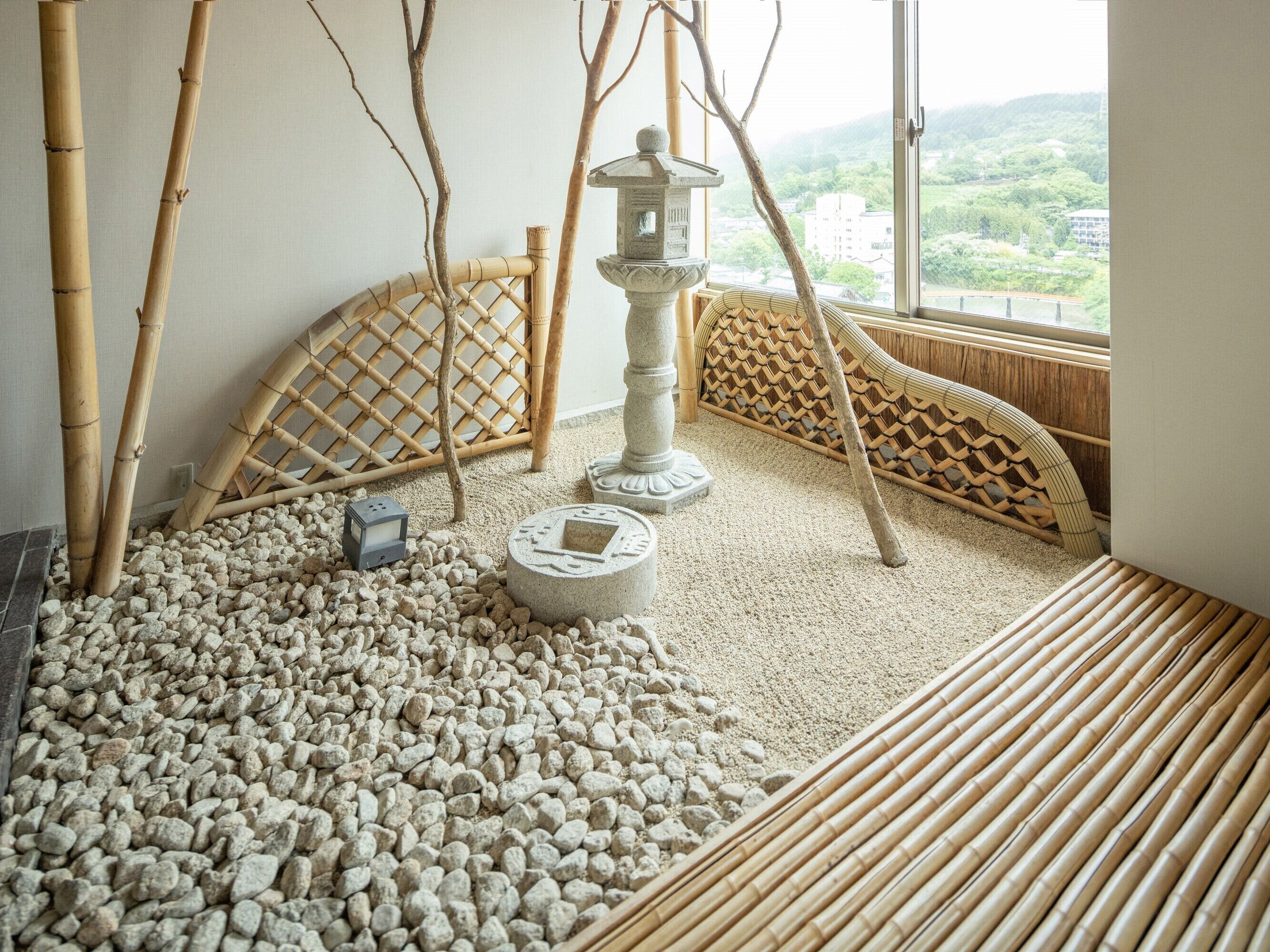 Una habitación con suelo de esterilla de tatami, un farol de piedra y vistas a un paisaje verde a través de una ventana.