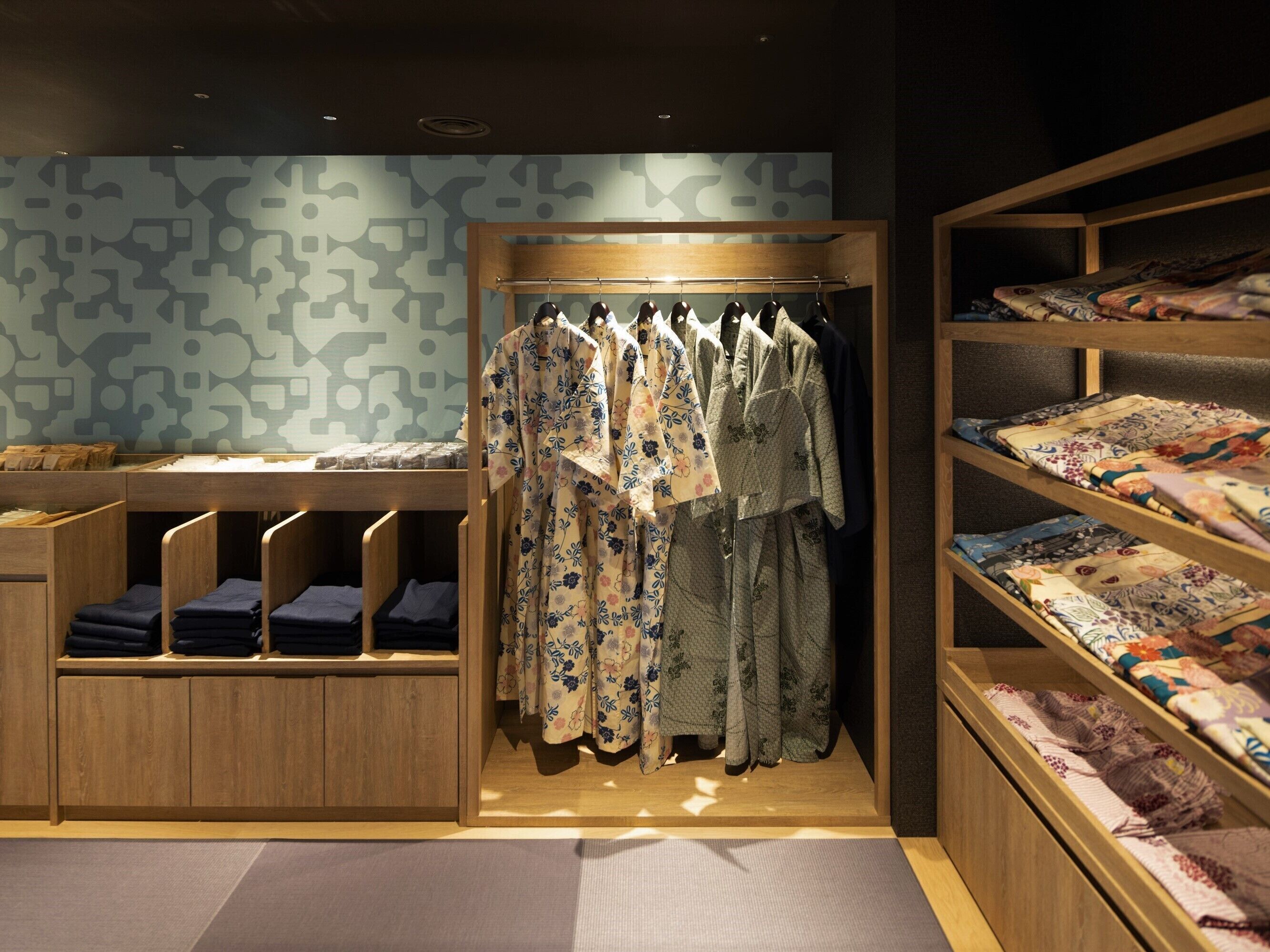 A neatly organized room with a clothing rack, shelves with folded textiles, and a patterned wall.