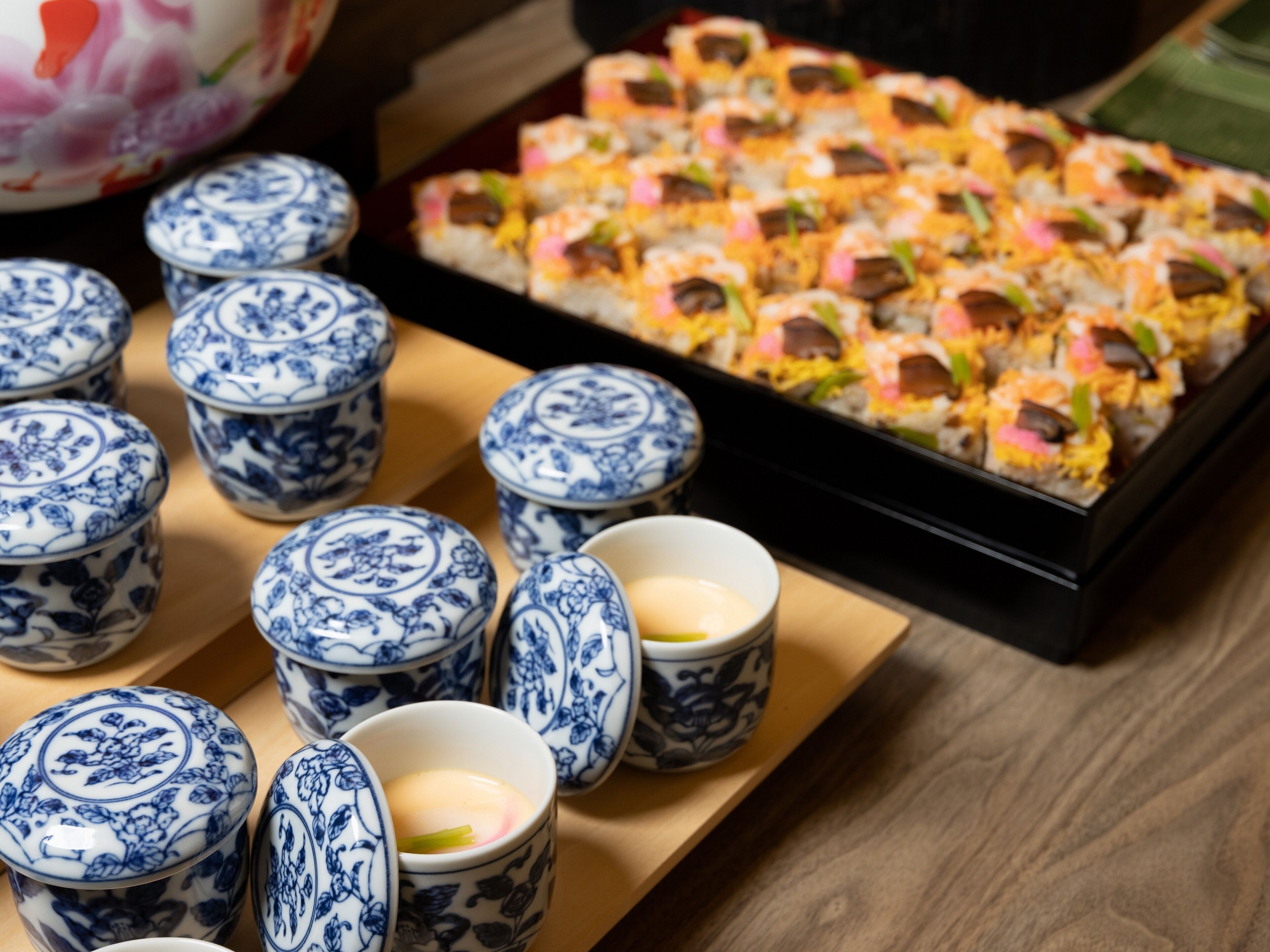 A tray of sushi and several blue and white ceramic cups on a wooden table.