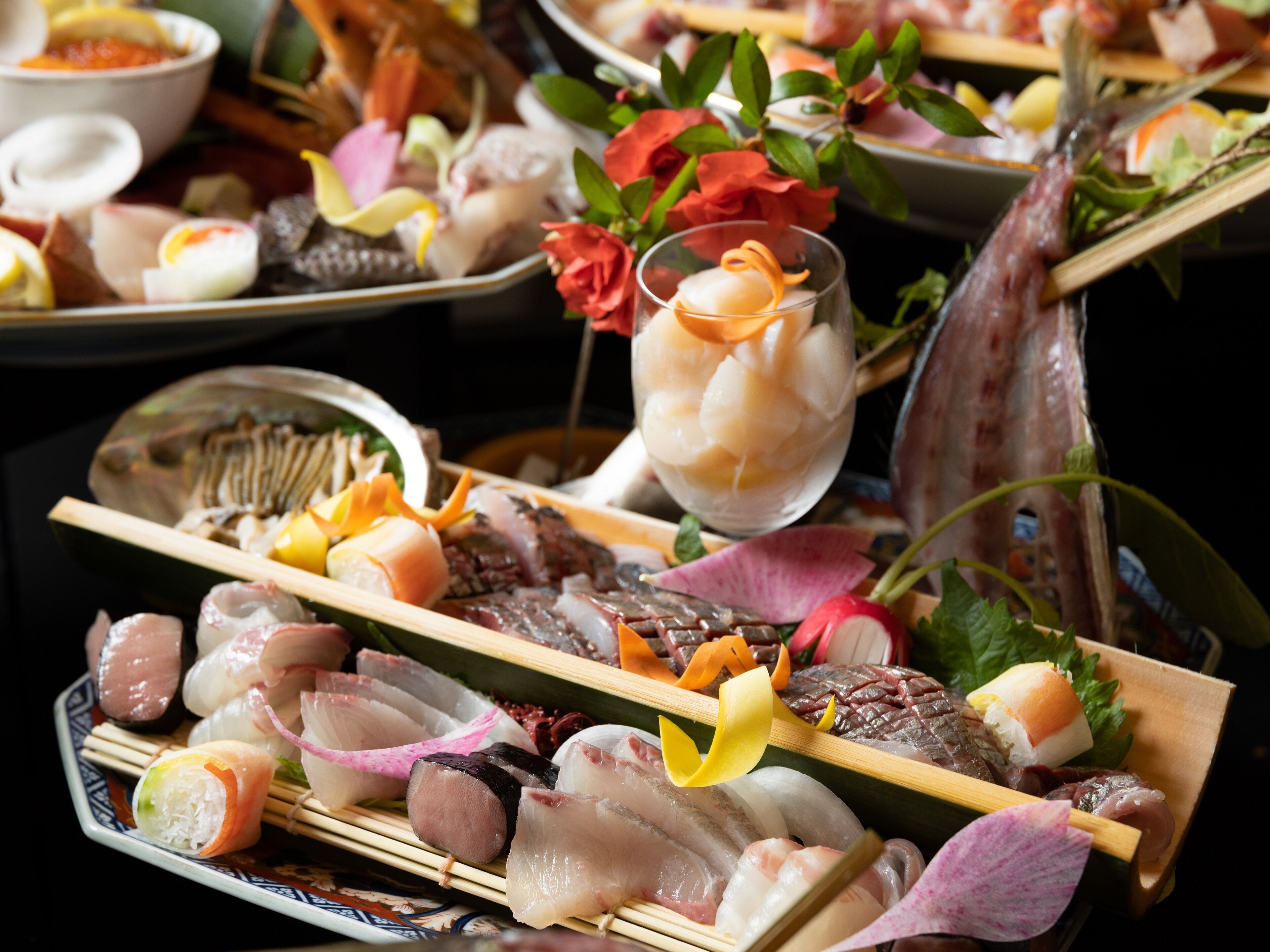 Une variété de sushis et de sashimis présentés sur des plateaux en bois, accompagnés d'un verre de boisson fraîche et de quelques fleurs décoratives.