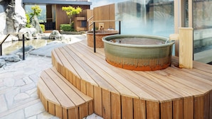 A wooden deck with a hot tub, a stone pathway, and a modern building with large windows. - HOTEL SAKURA URESHINO (Ureshino)