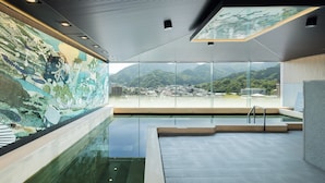A modern indoor swimming pool with a glass wall offering a view of a mountainous landscape. - HOTEL SAKURA URESHINO (Ureshino)