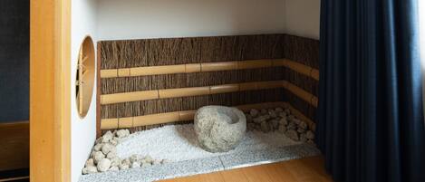 Una habitación tradicional japonesa con suelo de tatami, una batea de piedra y un muro de celosías de bambú.