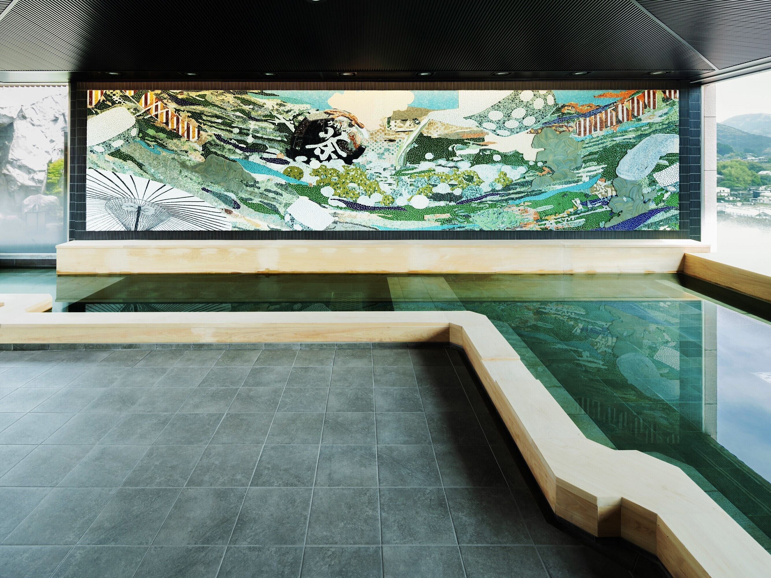 Un área de piscina interior moderna con un amplio mural de mosaicos en la pared, una piscina cristalina y una terraza de madera.