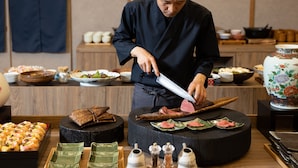 A chef slicing meat on a wooden board, surrounded by various dishes and condiments. - HOTEL SAKURA URESHINO (Ureshino)