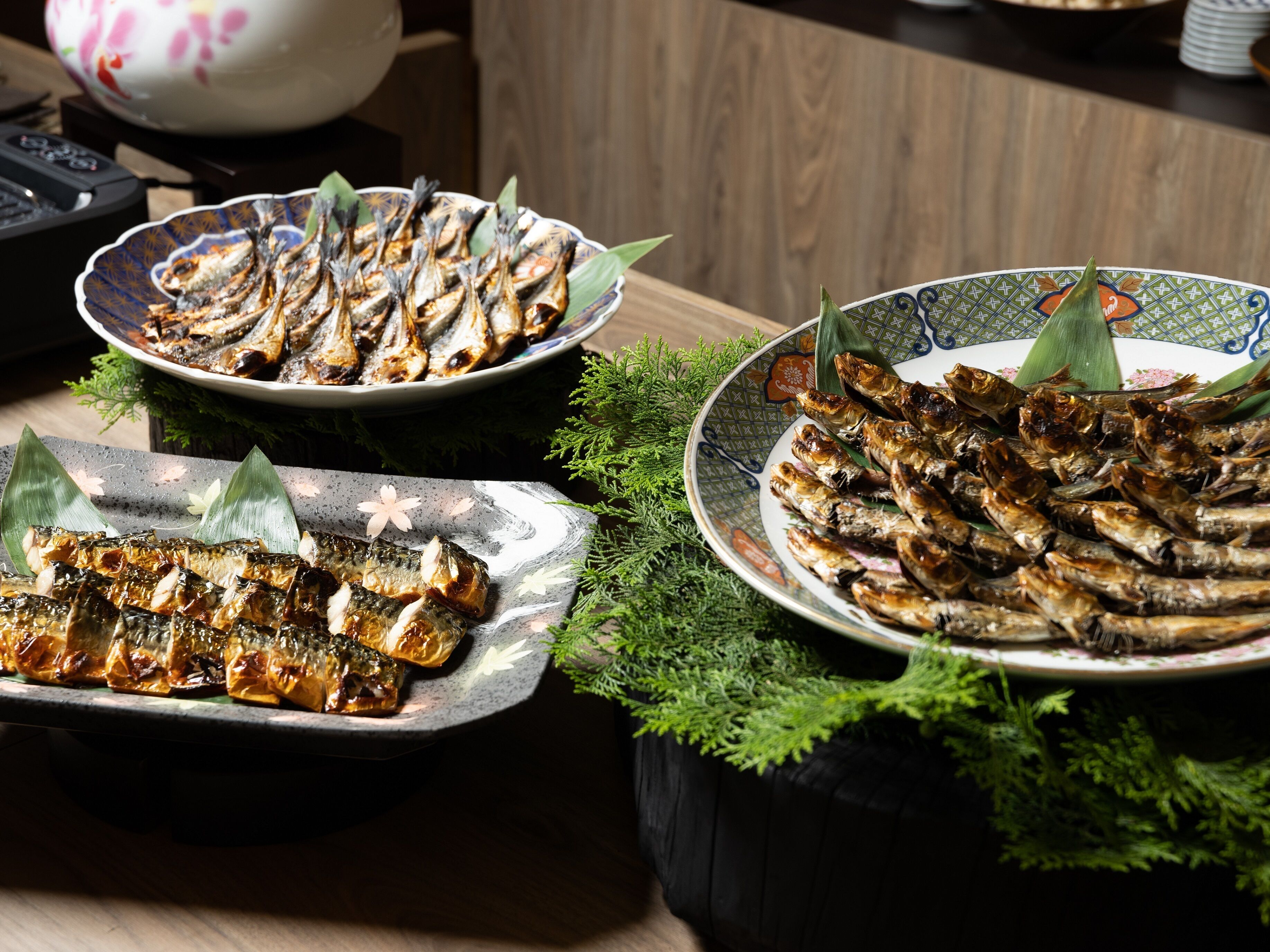A table with three plates of grilled fish, garnished with leaves.