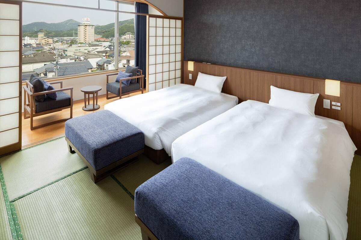 A hotel room with two beds, a view of the city, and traditional Japanese decor.