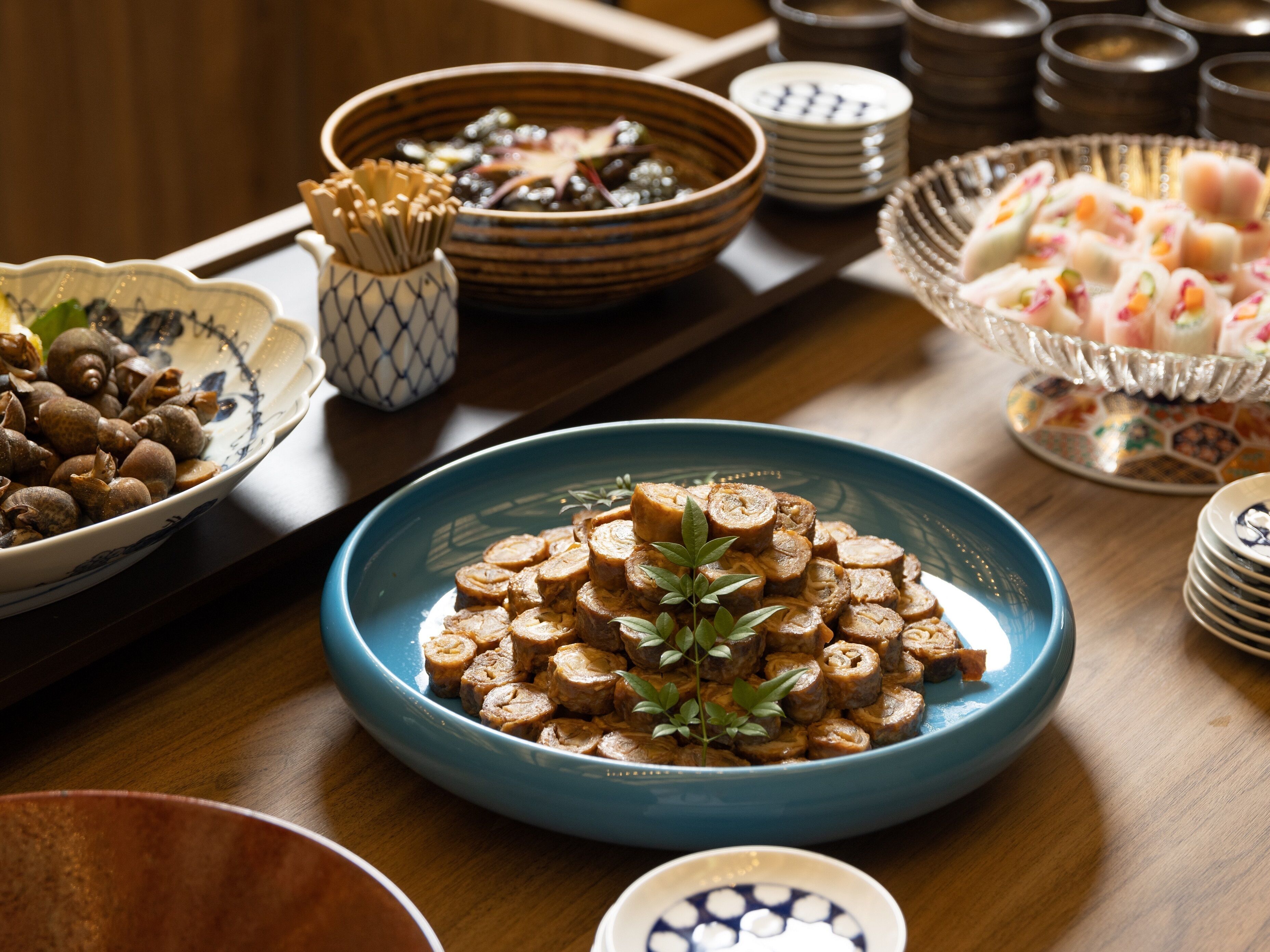 A table with various dishes, including a blue bowl with sliced meat and a bowl of nuts.