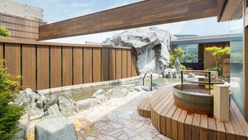 A modern outdoor spa area with a hot tub, stone pathway, wooden deck, and a large rock formation.