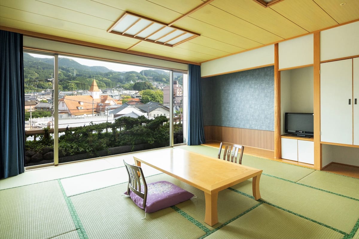 A traditional Japanese room with tatami flooring, a low wooden table, a cushioned bench, and a television on a shelf.