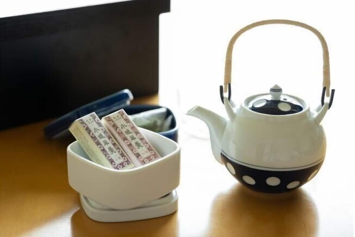 A white teapot with a black handle and a white bowl with a blue lid on a wooden surface.