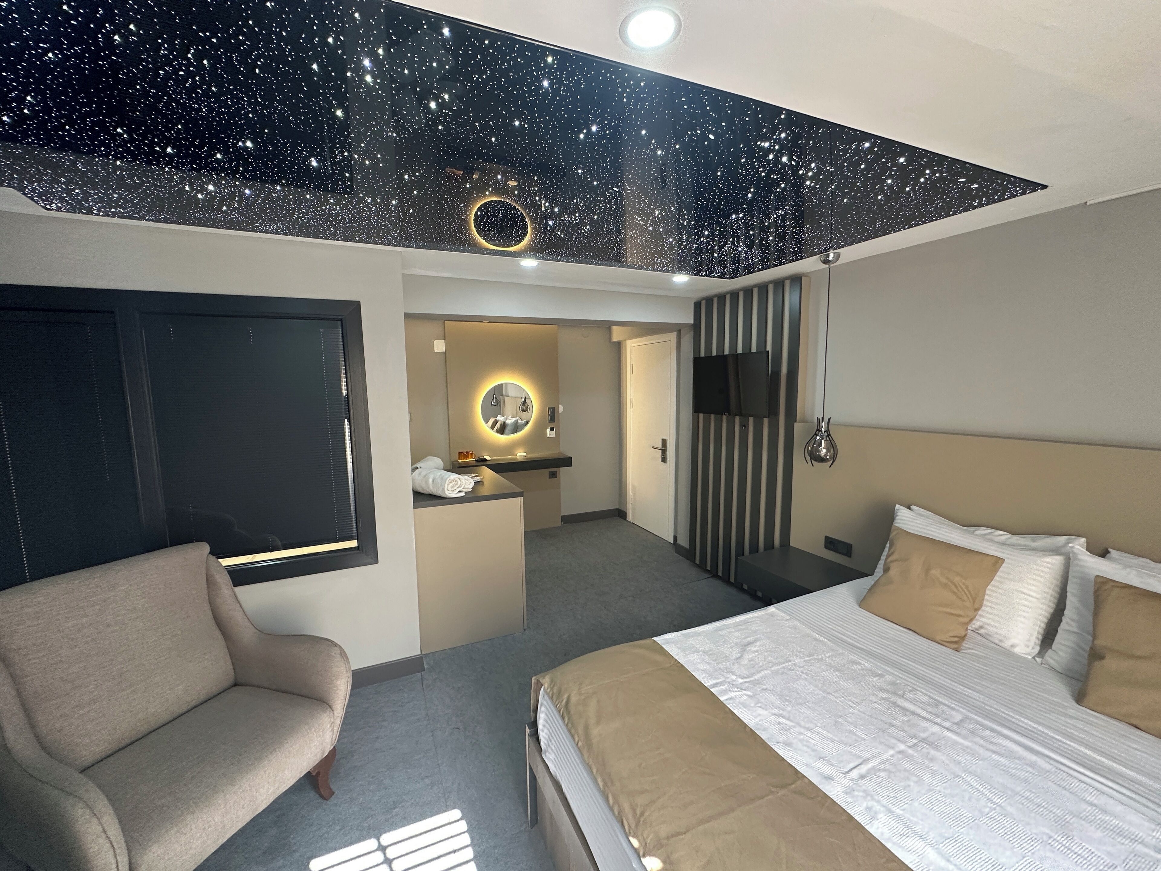 A hotel room with a bed, a sofa, a TV, and a ceiling with a starry design.