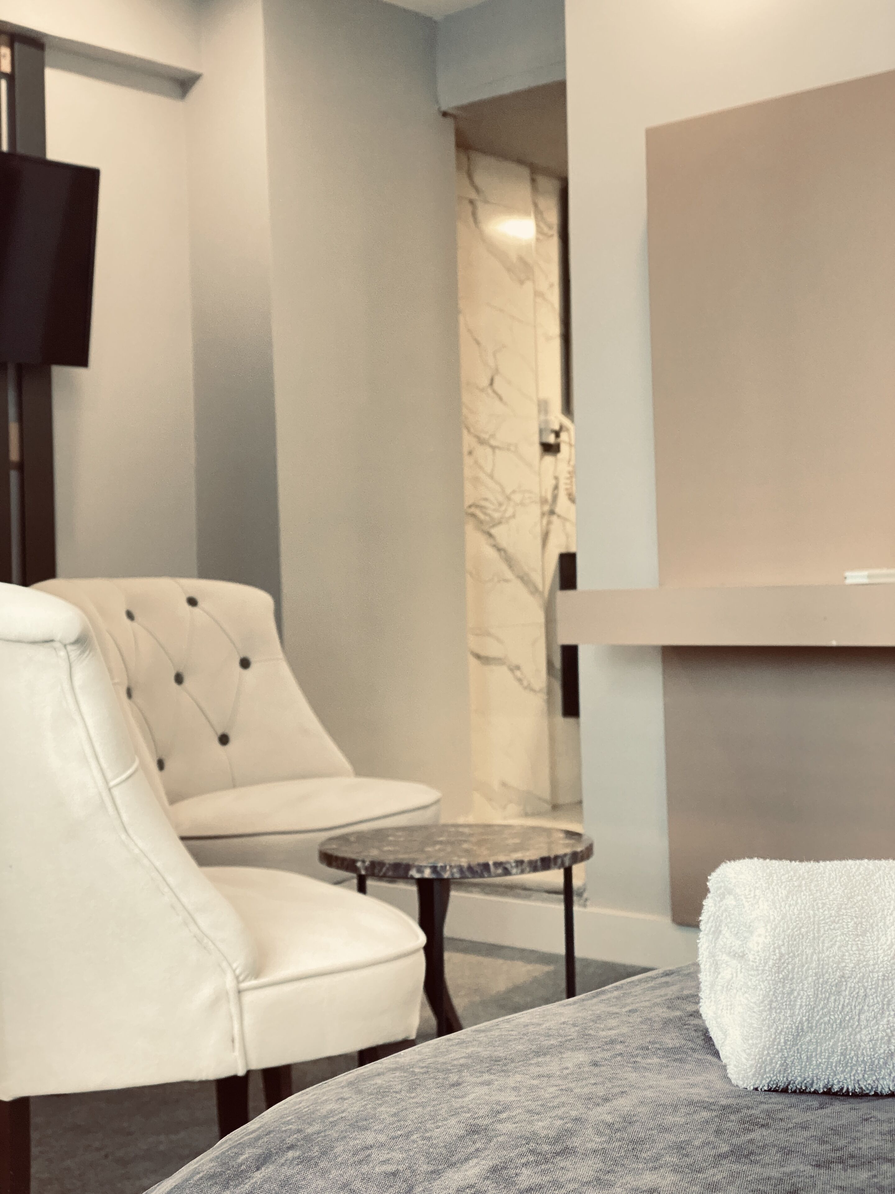 Una habitación de hotel moderna con un sillón de cuero blanco, una mesita redonda pequeña, una toalla blanca y una pared de mármol.
