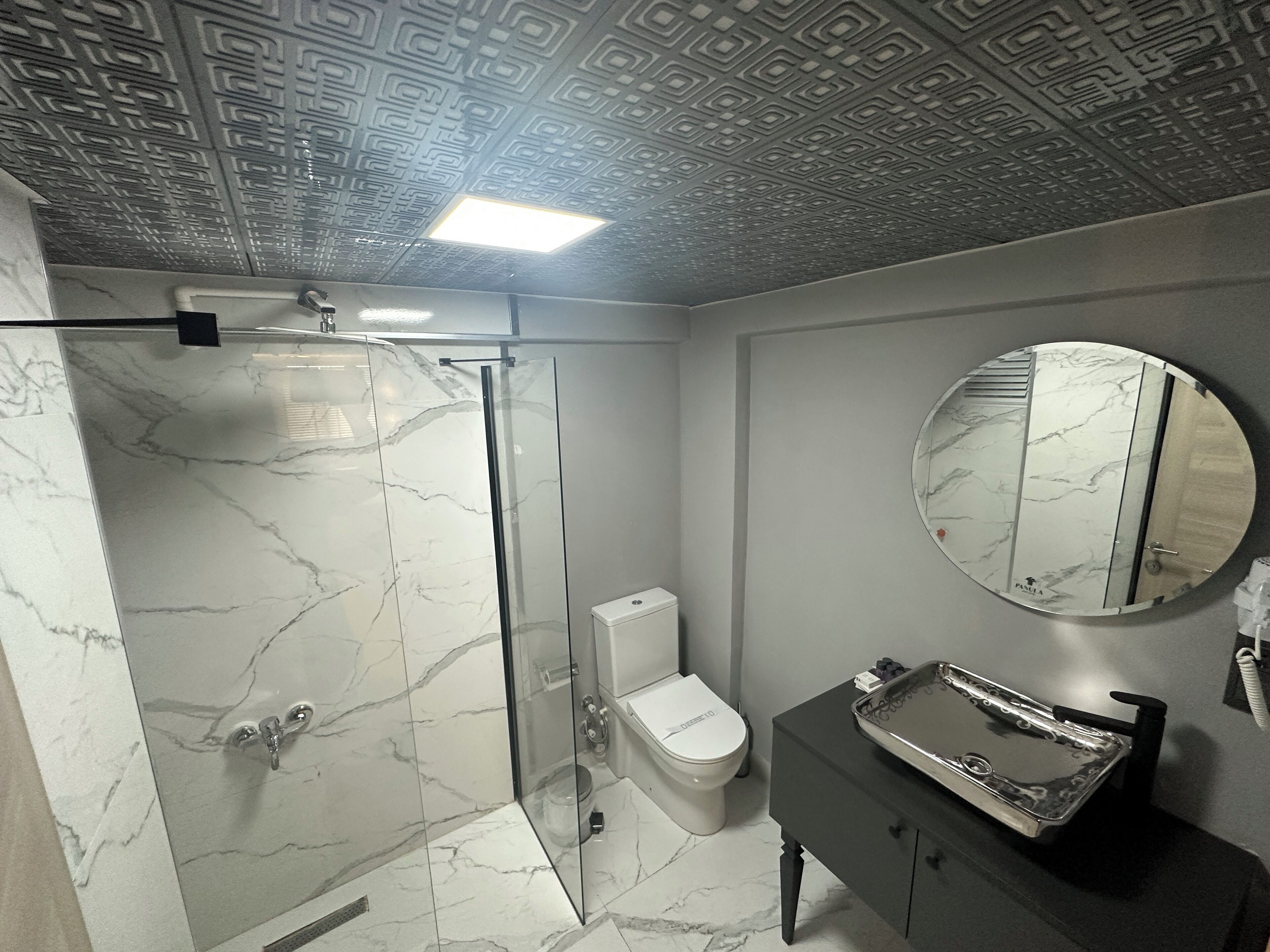A bathroom with a glass-enclosed shower, a toilet, a sink with a mirror, and a marble floor.
