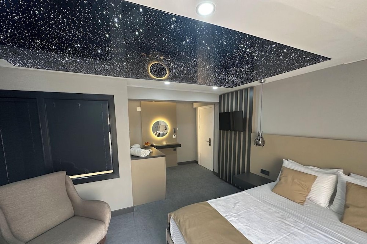 A hotel room with a bed, a sofa, a desk, a mirror, and a TV.